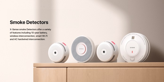 Three X-Sense smoke detectors displayed on a wooden surface, showcasing their sleek designs and features like wireless interconnection and Wi-Fi capabilities.