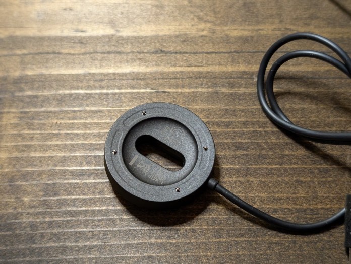 Close-up of a magnetic charging dock for a smartwatch, featuring a circular design with a central slot and attached cable on a wooden surface.
