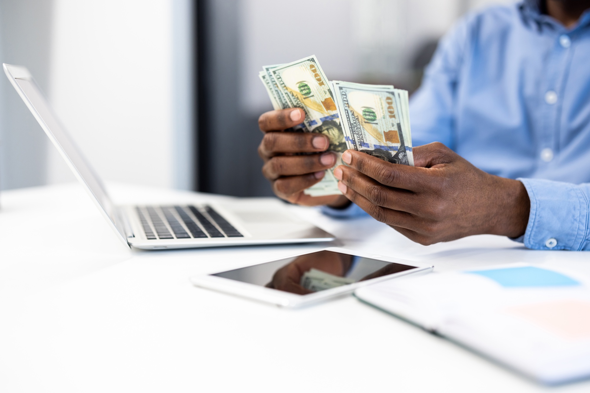 Business person counting cash at office desk with laptop, phone, and documents for financial
