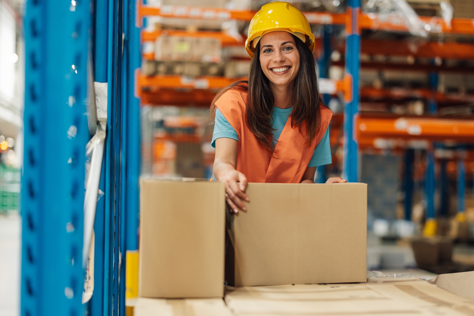 Smiling female warehouse worker with box on an industrial shelf