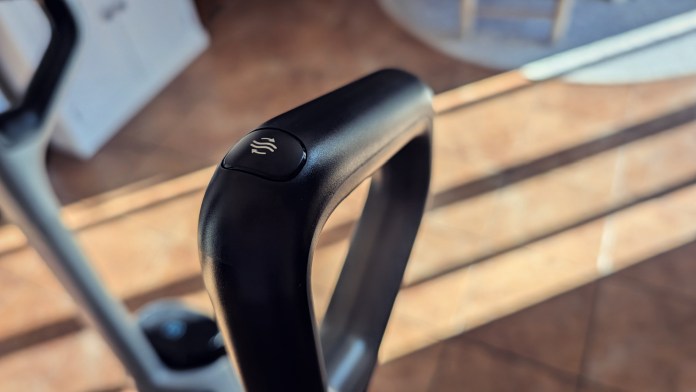 Close-up of the handle of a modern wet/dry vacuum cleaner, featuring a button with a water droplet symbol, capturing sunlight and shadows on a tiled floor.