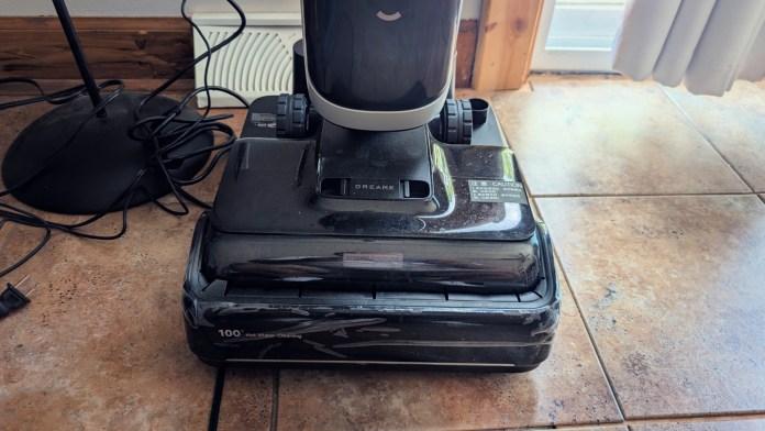 A close-up view of a Dreame H15 Pro Heat wet/dry vacuum positioned on a tiled floor, with visible power cord and nearby lamp.