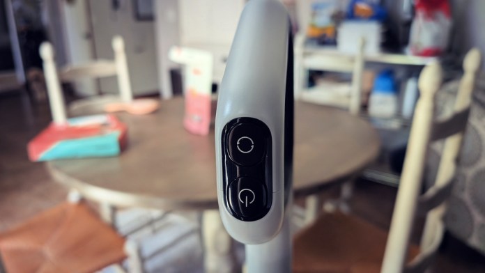 Close-up of a control panel on a wet/dry vacuum, featuring two buttons, set against a blurred background of a kitchen dining area.