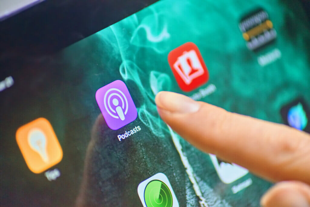 finger hovering over an iphone screen right above the apple podcasts app icon