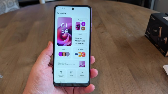 A person holding a smartphone displaying a customizable settings screen with time, themes, fonts, and color options.