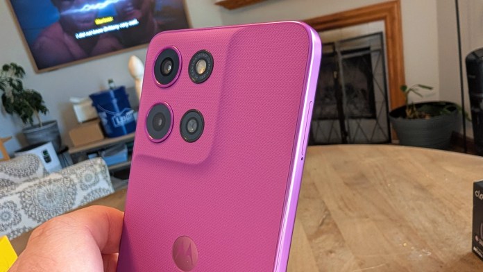 A close-up view of a purple Motorola smartphone being held, showcasing its rear design and triple camera setup.